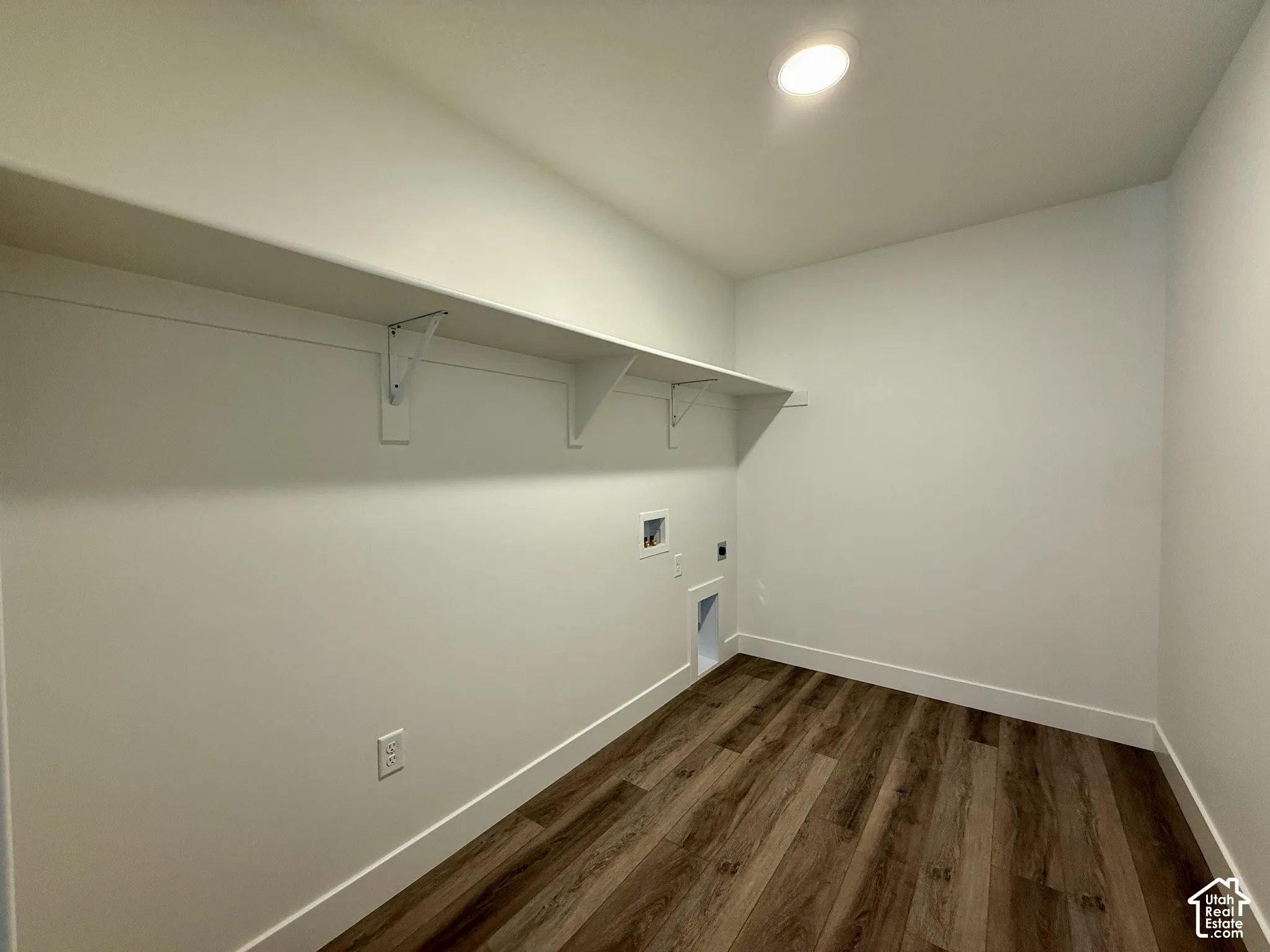 Utility space featuring wood-finish flooring, a full-length wall-mounted shelf with support brackets, and recessed ceiling lighting