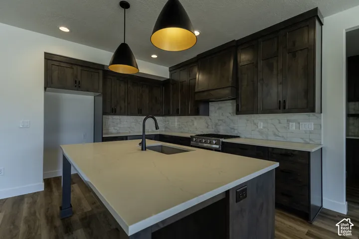 Kitchen featuring a center island with undermount sink, dark wood-finish cabinetry, stainless steel range, and subway tile backsplash