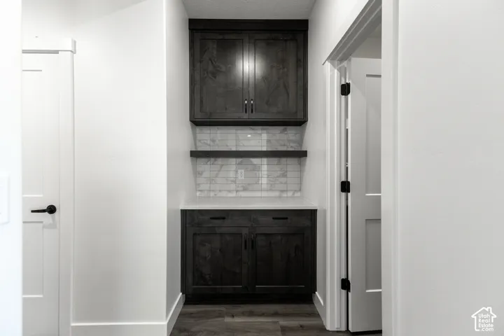 Cabinetry with a wood-finish, white countertop, tile backsplash, and wall-mounted shelving