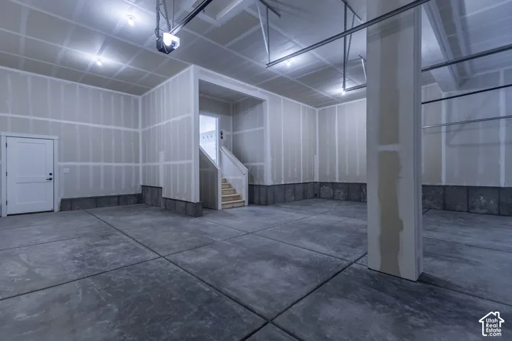 Concrete flooring, white interior door, exposed ceiling joists, garage door opener