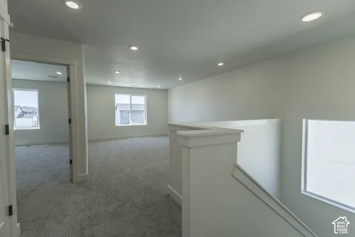 Open loft space with recessed lighting, light-toned carpeting, and multiple windows