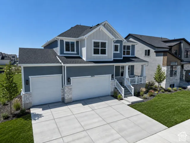 Two-story residence featuring a two-car garage, stone and siding exterior, front porch with white railings, and a concrete driveway