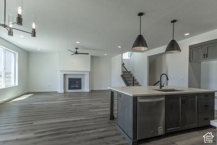 Open-concept living space featuring wood-finish flooring, a fireplace with a white mantel, and an island with a built-in sink and dishwasher