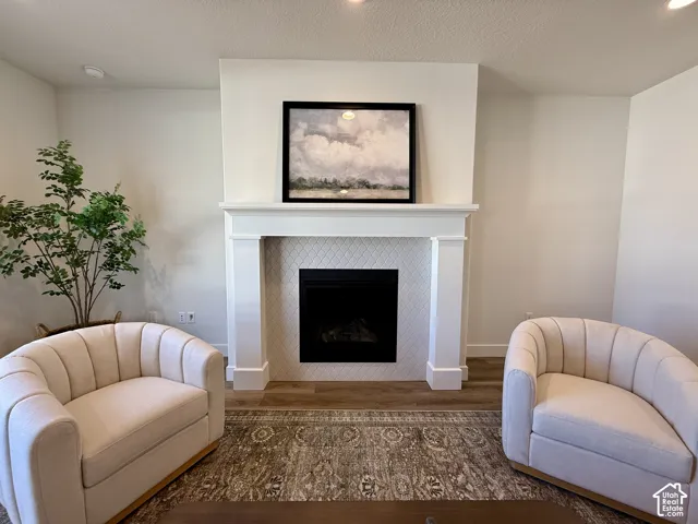 Fireplace featuring a white mantel, diamond-patterned tile surround, and wood-finish flooring