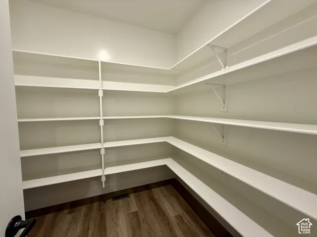 Walk-in pantry featuring white wrap-around shelving and wood-finish flooring