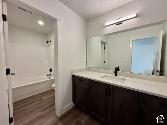 Bathroom featuring dark wood-finish cabinetry, solid-surface countertop with an integrated rectangular basin, matte black fixtures, full-width vanity mirror, and wood-finish flooring