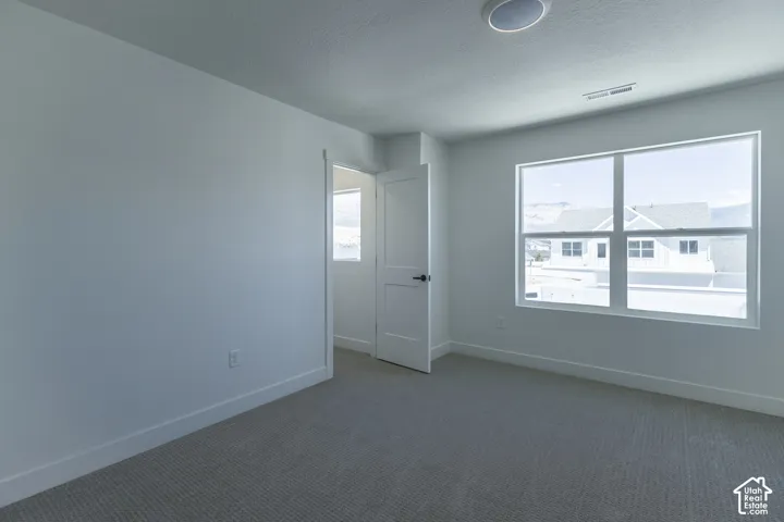 Spacious room with light-colored carpeting, white painted walls, and a large multi-pane window