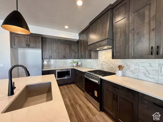 Kitchen featuring dark-stained cabinetry, quartz countertops, a stone-patterned tile backsplash, wood-finish flooring, and a matte black pendant light fixture over a center island