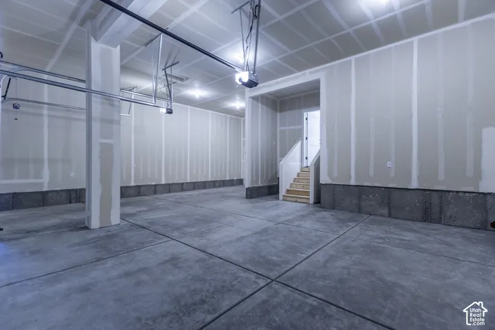 Spacious garage featuring a concrete floor, exposed drywall, and an interior staircase