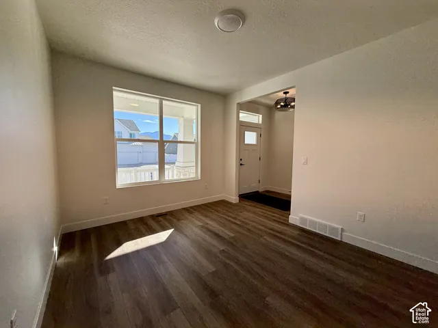 Room featuring wood-finish flooring, a large picture window, and a multi-light flush-mount ceiling fixture, with visibility of an entry door and transom window