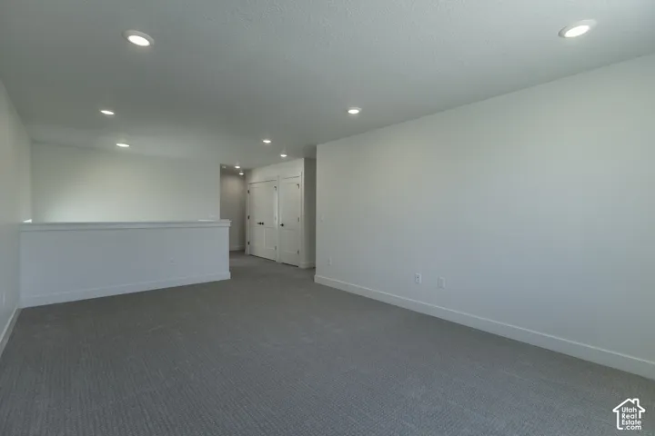 Expansive carpeted area with recessed lighting, white walls, and a white railing