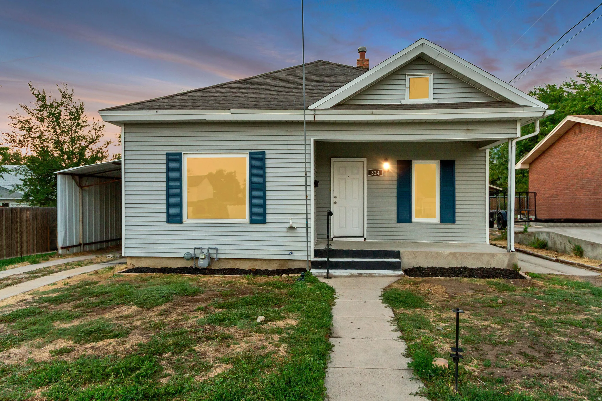 Light gray horizontal siding, dark asphalt shingle roof, covered front porch, white entry door with black handle, and dark blue window shutters