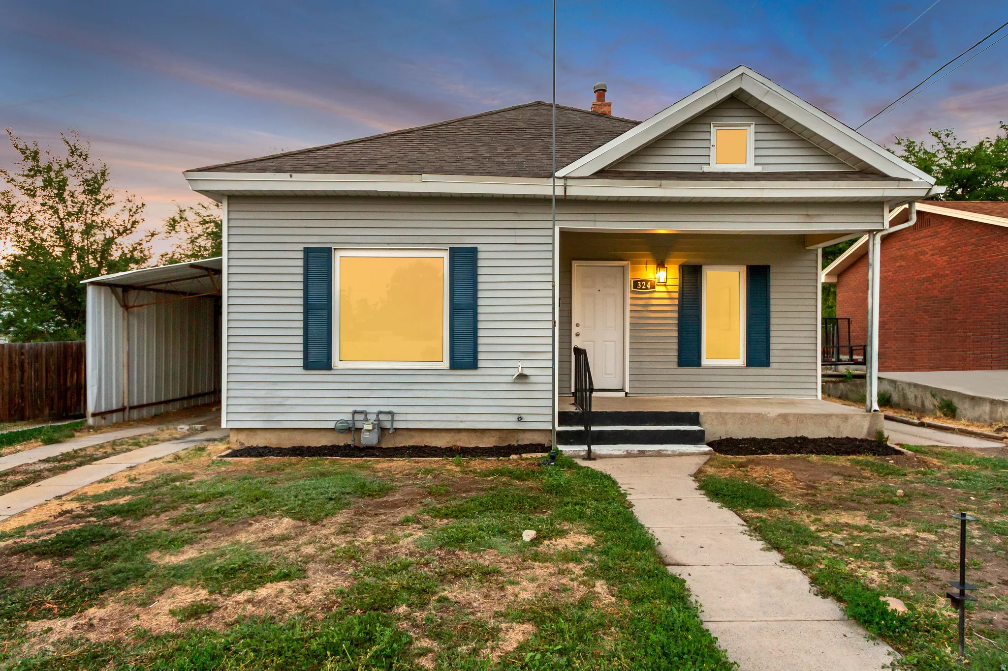 Covered front porch with light fixture, vinyl siding, asphalt shingle roof, and a detached carport