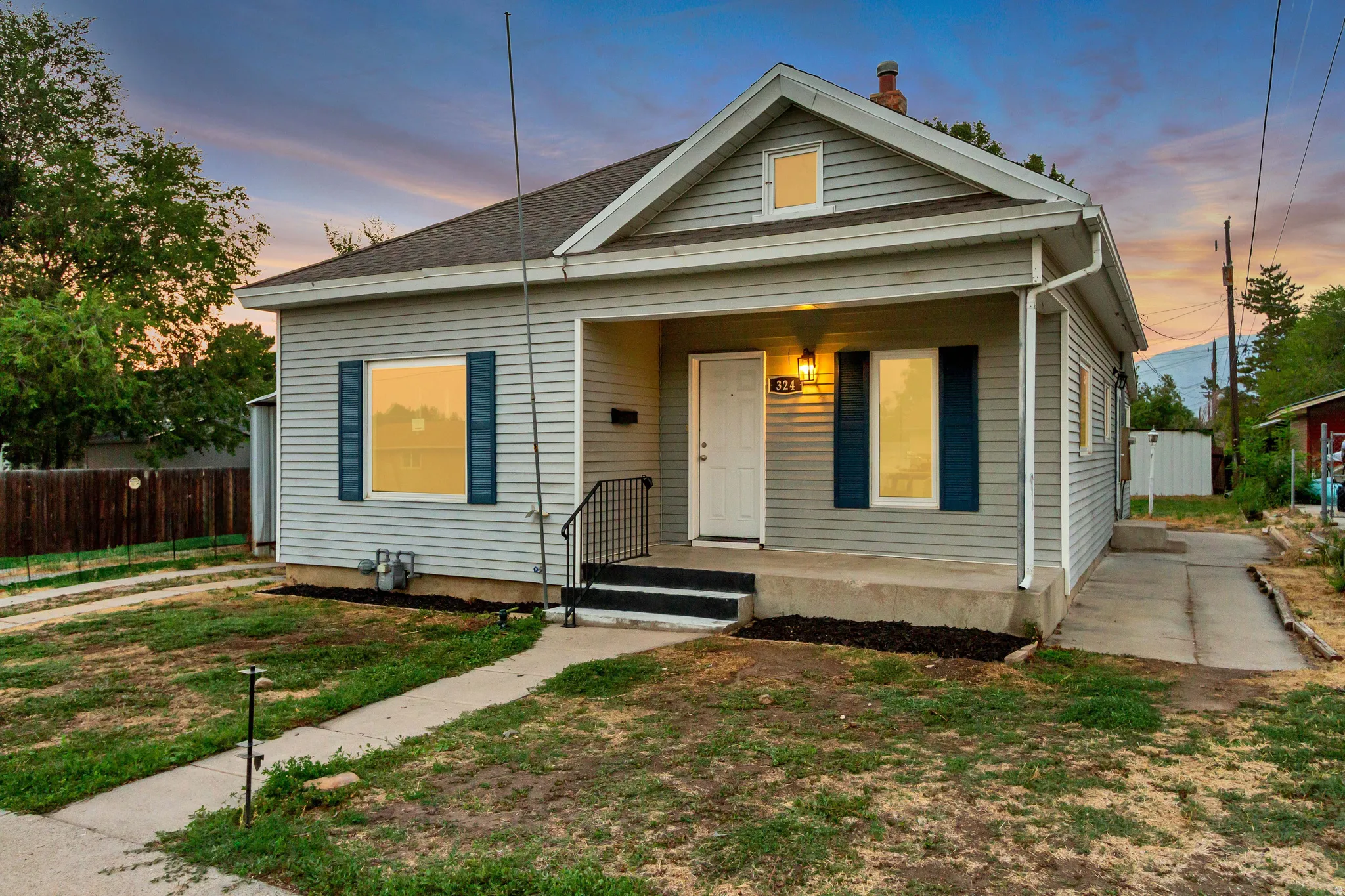 Siding exterior with blue window shutters, covered front porch, concrete front steps with wrought iron railing, and a concrete driveway