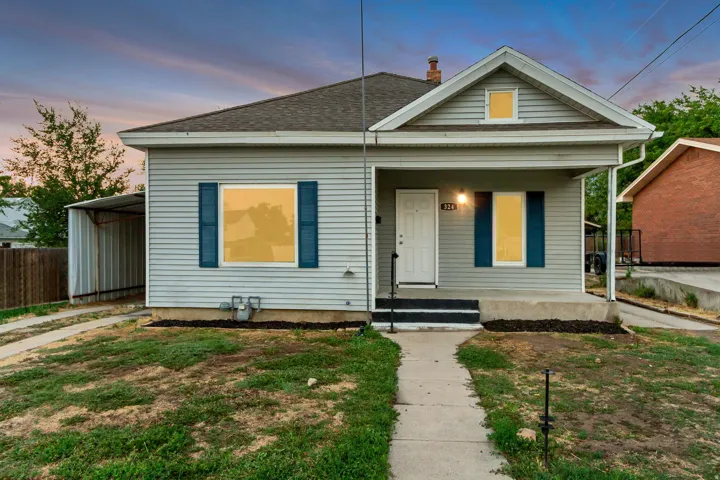 Light gray horizontal siding, dark asphalt shingle roof, covered front porch, white entry door with black handle, and dark blue window shutters
