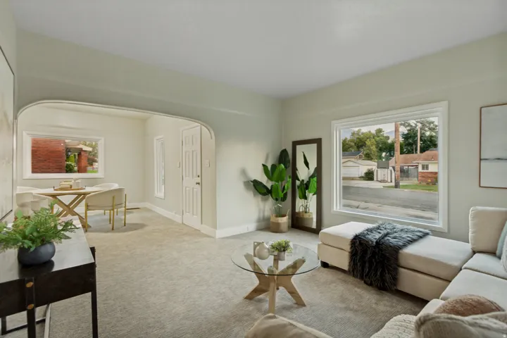 Spacious living area with neutral carpeting, large windows, and an arched doorway leading to an additional room