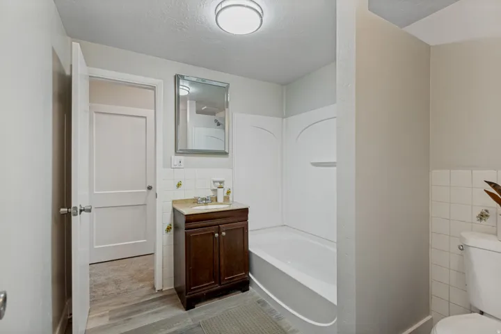Bathroom featuring a dark wood-finish vanity with a light countertop, a built-in bathtub with a shower surround, and wood-finish flooring