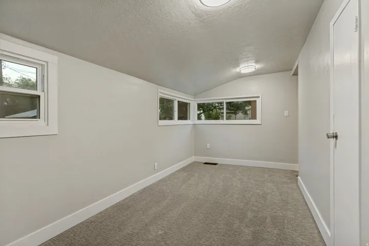 Neutral-toned walls with contrasting white trim, vaulted ceiling, two recessed lighting fixtures, and light gray carpeting