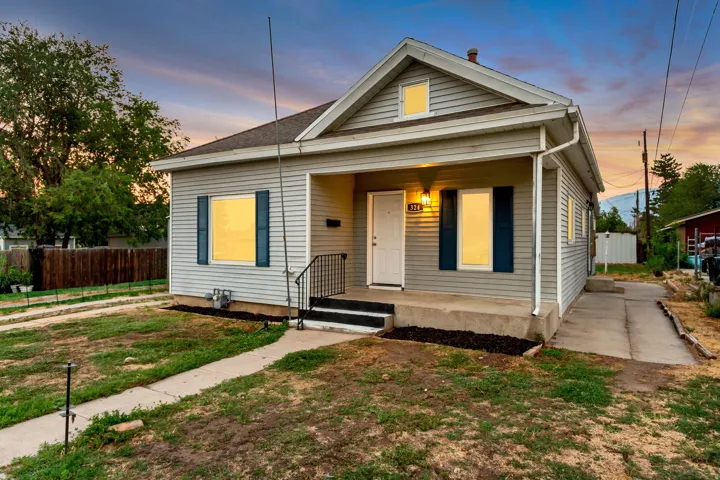 Light gray siding exterior with dark blue window shutters, covered front porch, white front door, and black wrought iron handrail