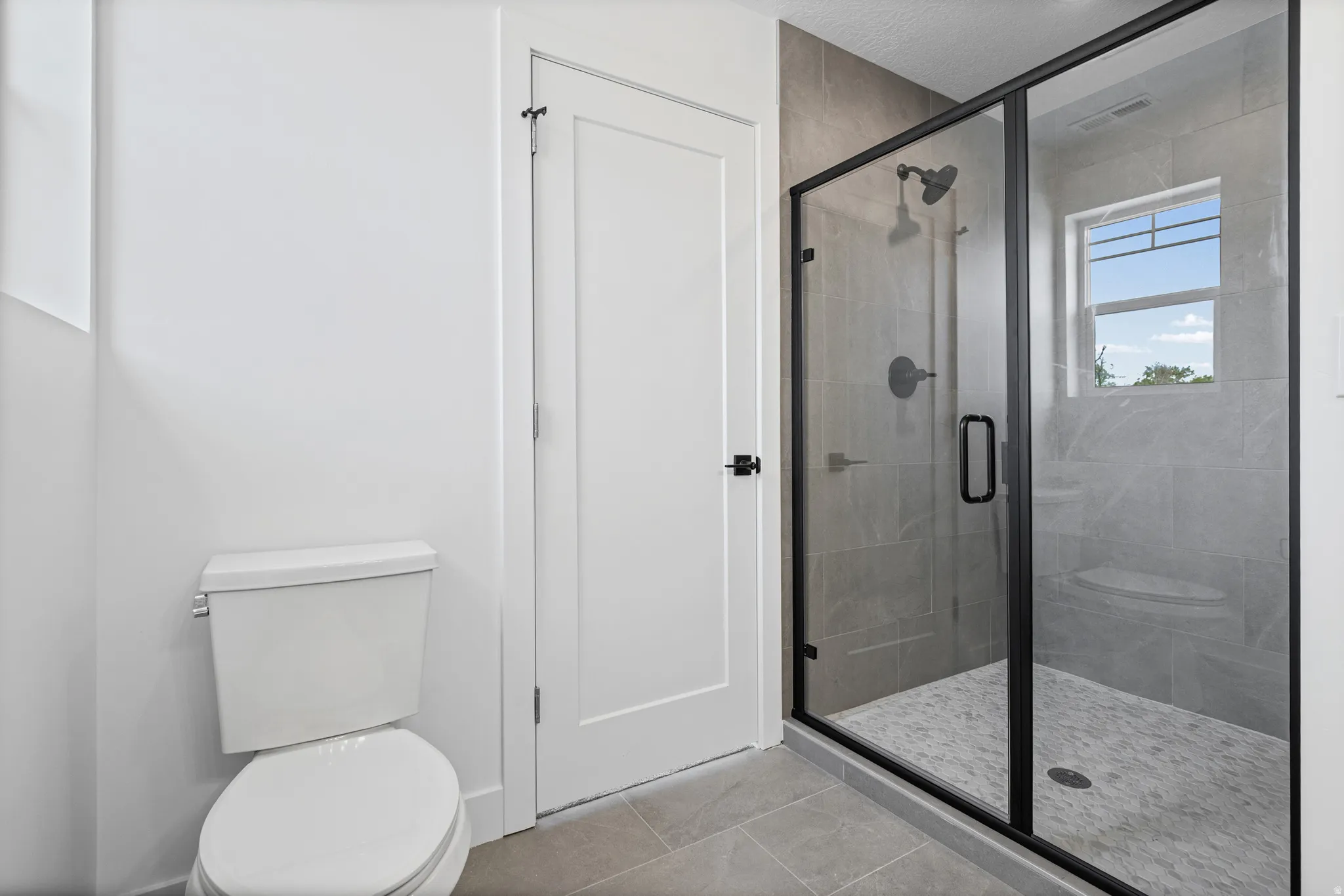 Walk-in shower with black-framed glass enclosure, grey tile surround, and built-in shower bench