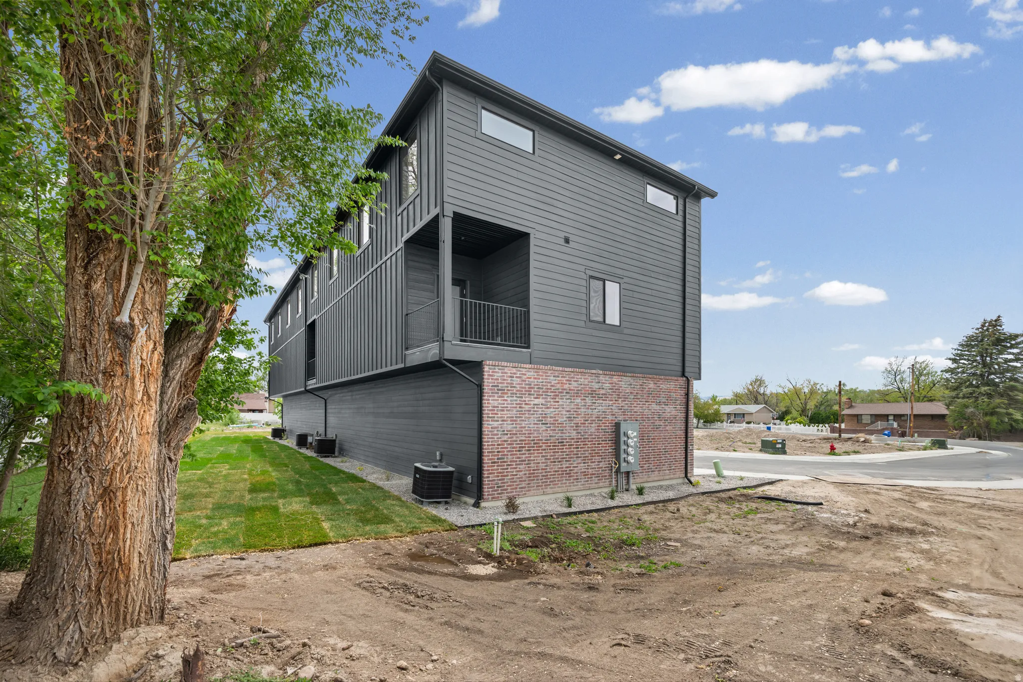 Modern facade with dark gray siding, brick veneer accent, multiple windows, and a private balcony