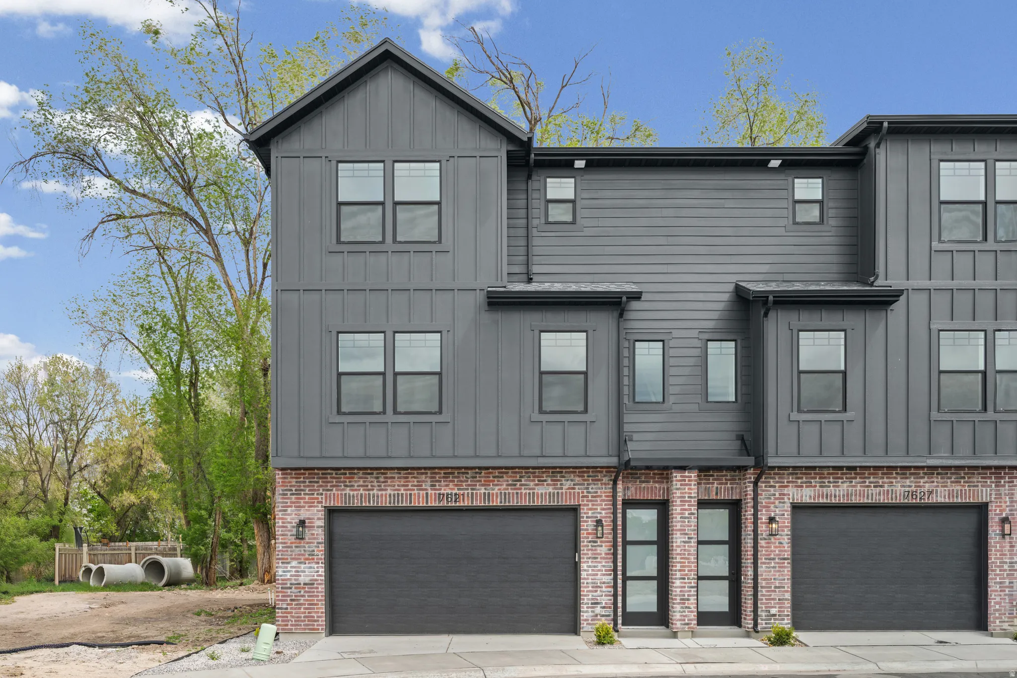 Contemporary multi-level exterior with board and batten siding, brick accents, dark-framed windows, and integrated garage doors