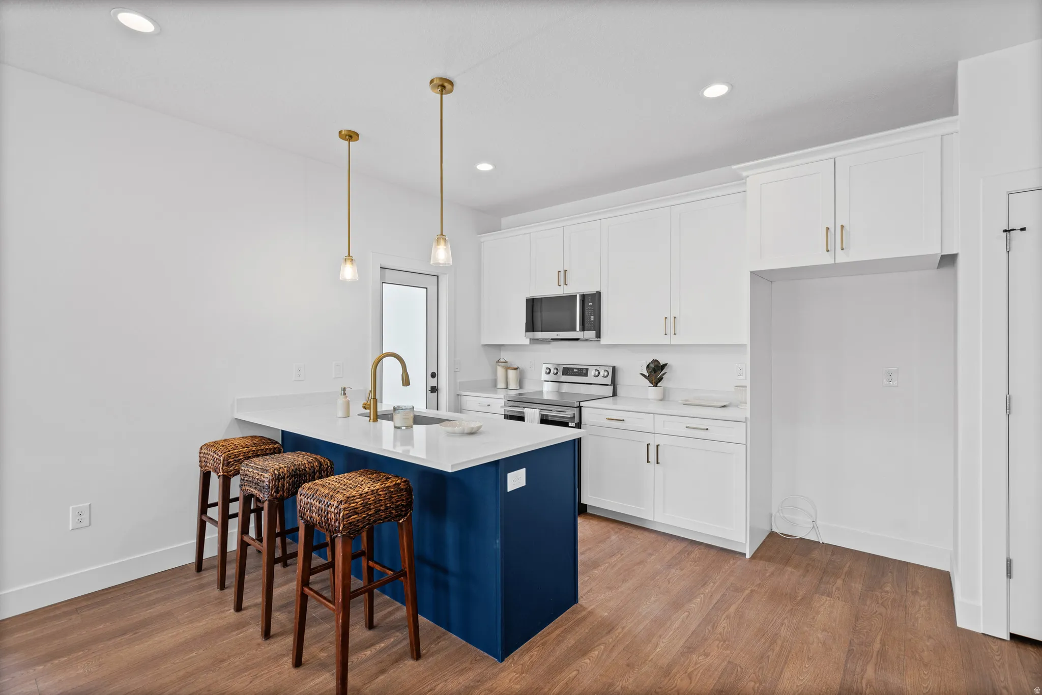 Kitchen featuring white cabinetry, wood-finish flooring, a blue island with a built-in sink, and pendant lighting