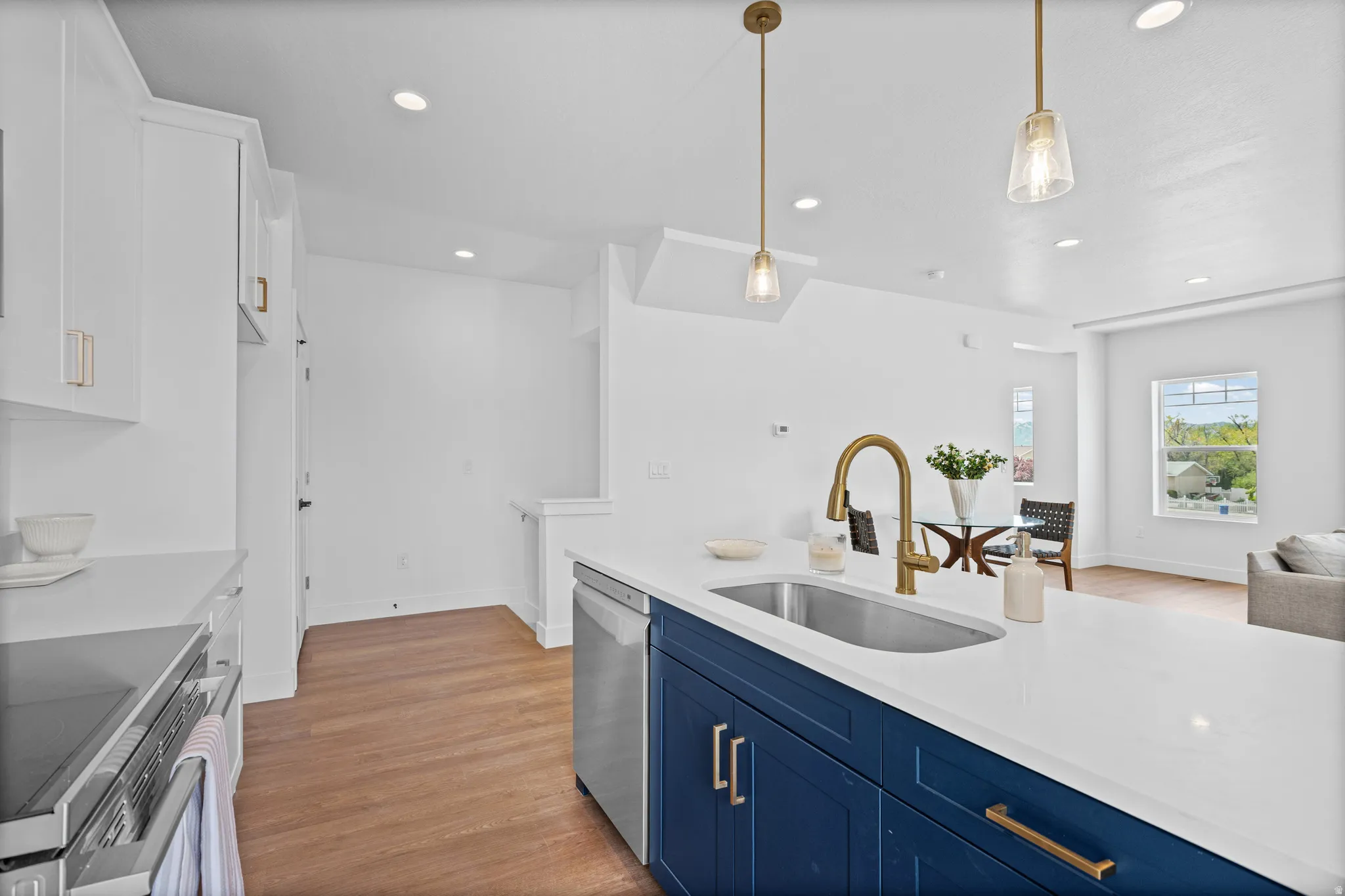 Kitchen featuring a deep blue island with a built-in sink and gold-tone faucet, white countertops, stainless steel dishwasher, and recessed lighting