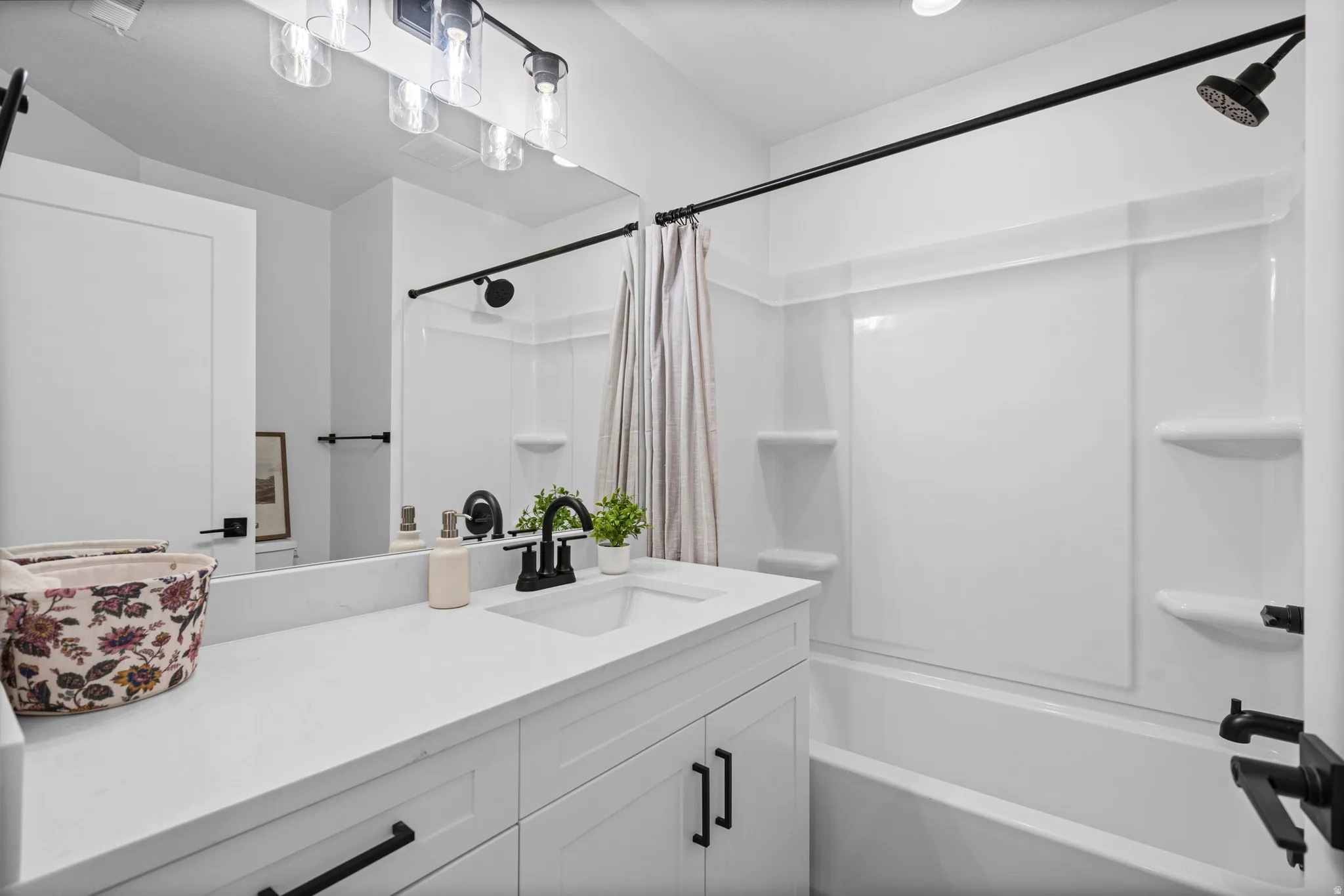 White vanity with a single basin sink and matte black faucet, featuring a matching countertop and under-sink cabinetry with black hardware