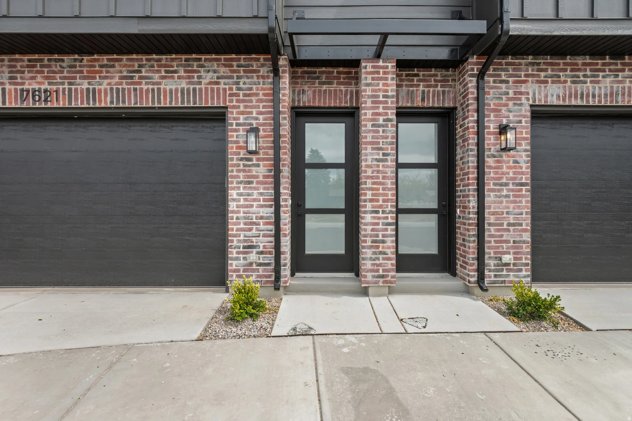 Brick facade with dark garage doors, modern entry doors featuring frosted glass panels, and exterior wall sconces