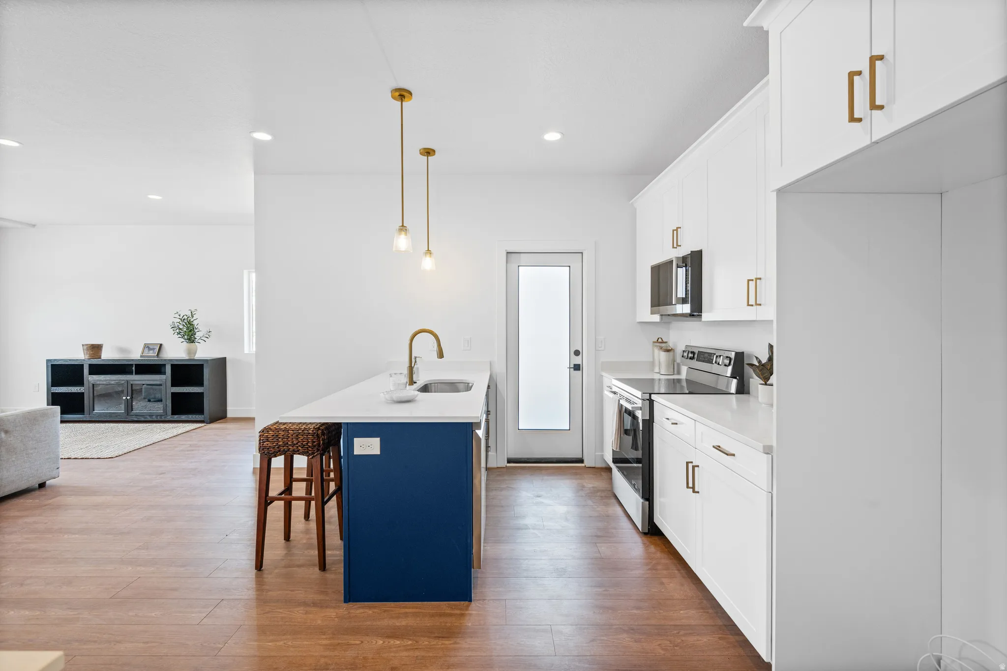 Kitchen featuring a blue island with a built-in sink, white cabinetry with gold-tone hardware, stainless steel appliances, and pendant lighting