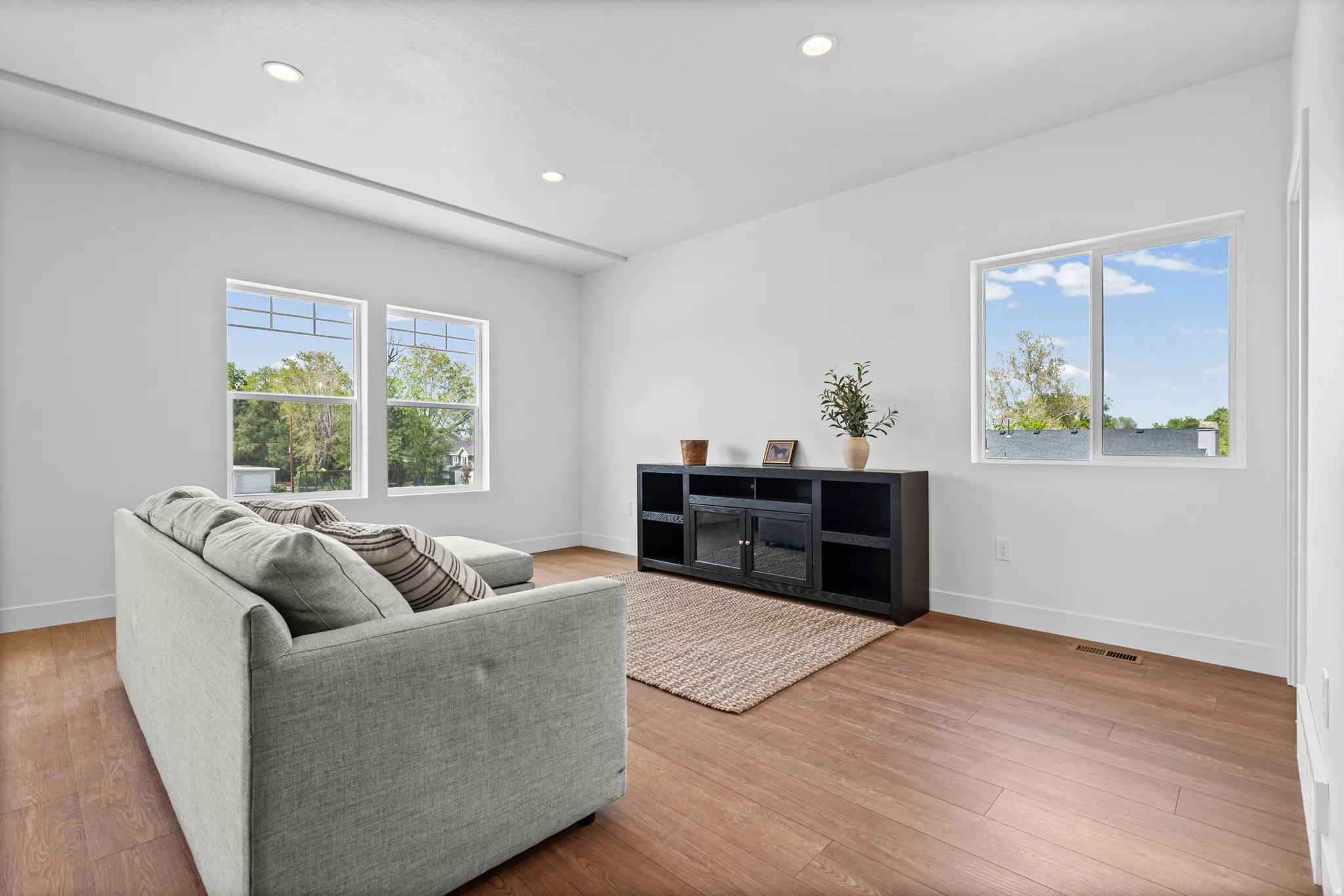 Recessed lighting illuminates the open living area featuring wood-finish flooring and multiple windows