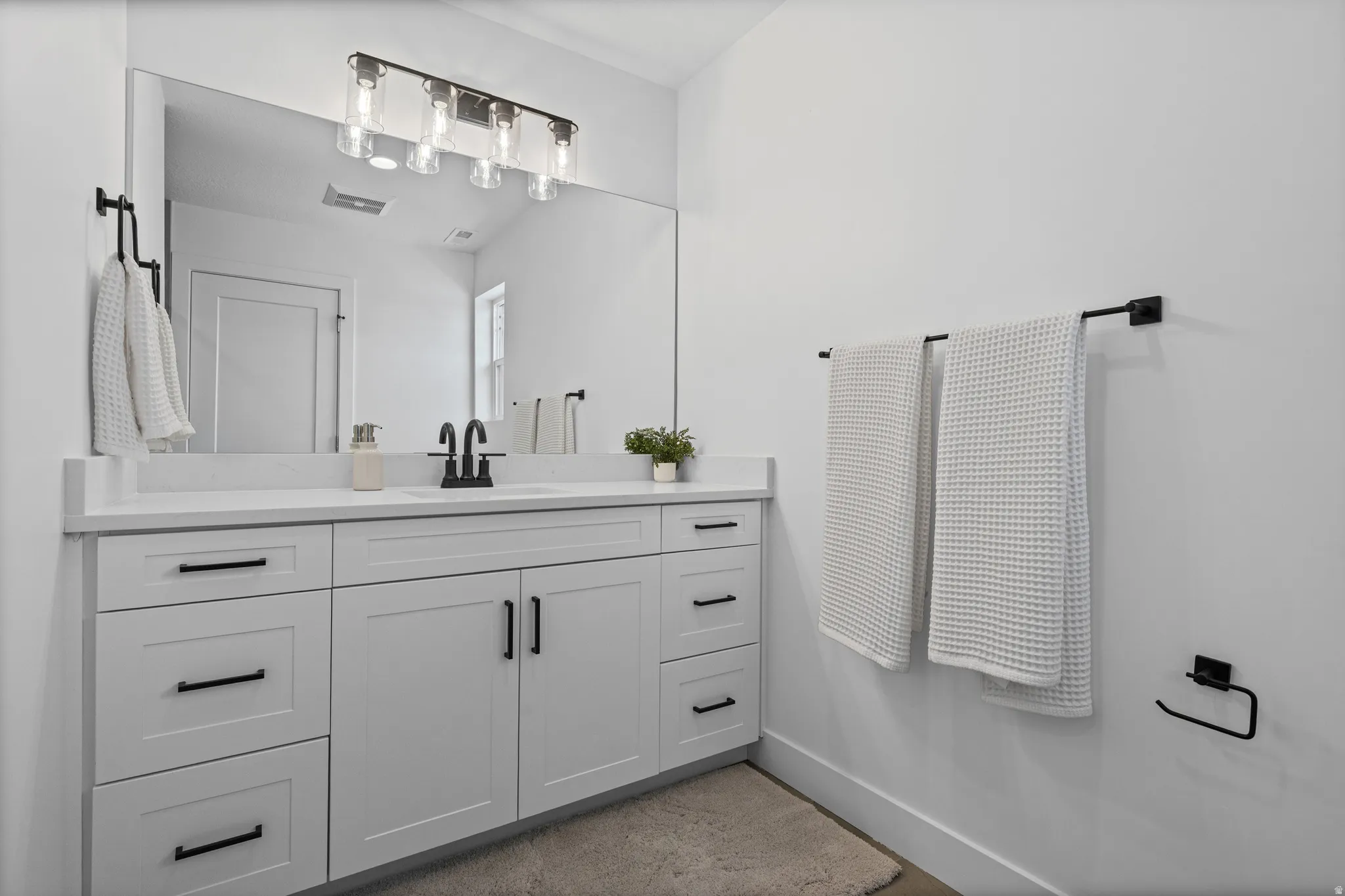 White vanity with shaker-style cabinetry, quartz countertop, and a black-finish faucet