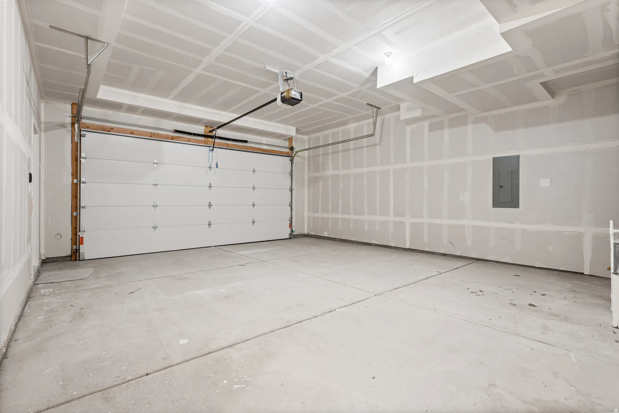 Spacious garage with an overhead door, automatic opener, concrete flooring, and unfinished drywall walls