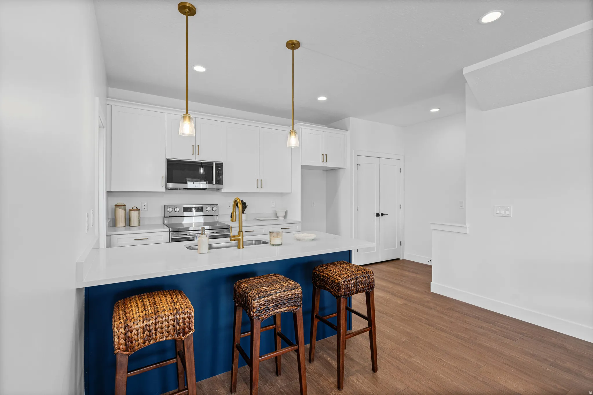 Contemporary kitchen featuring white cabinetry with brushed brass hardware, stainless steel appliances, and a striking navy blue island with woven rattan seating