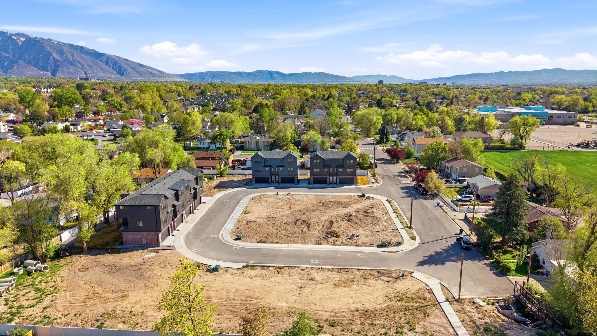 Newly paved streets, adjacent to developing residential structures, with established neighborhood trees and distant mountain ranges