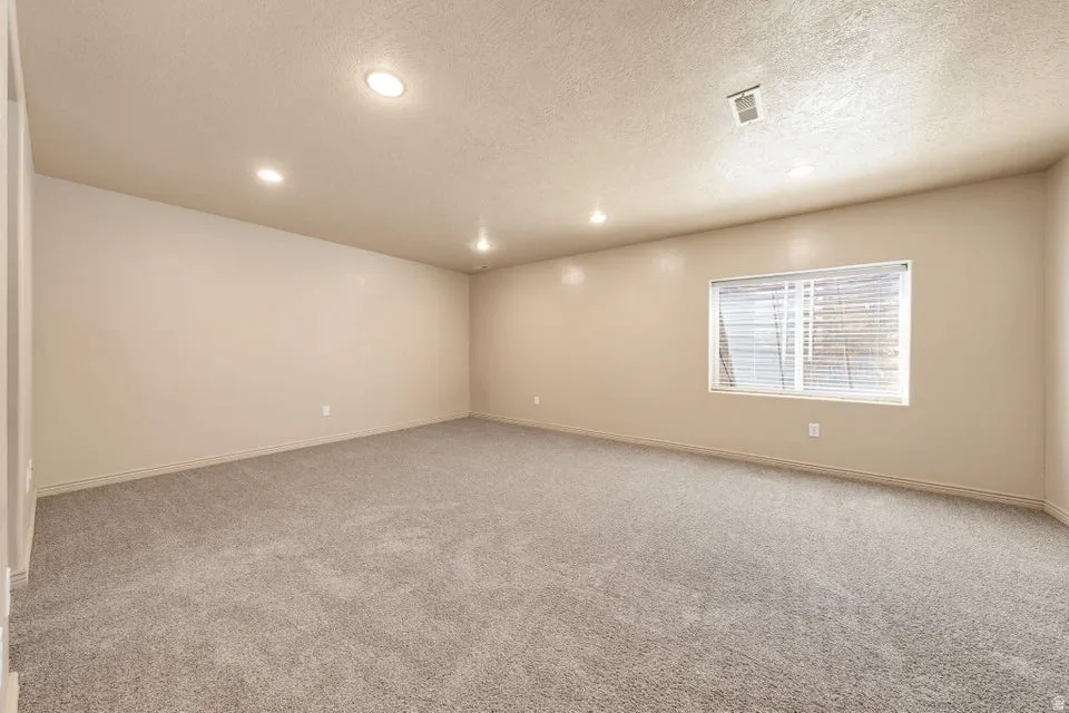 Spacious room featuring neutral wall paint, recessed ceiling lighting, textured ceiling, and gray carpet flooring