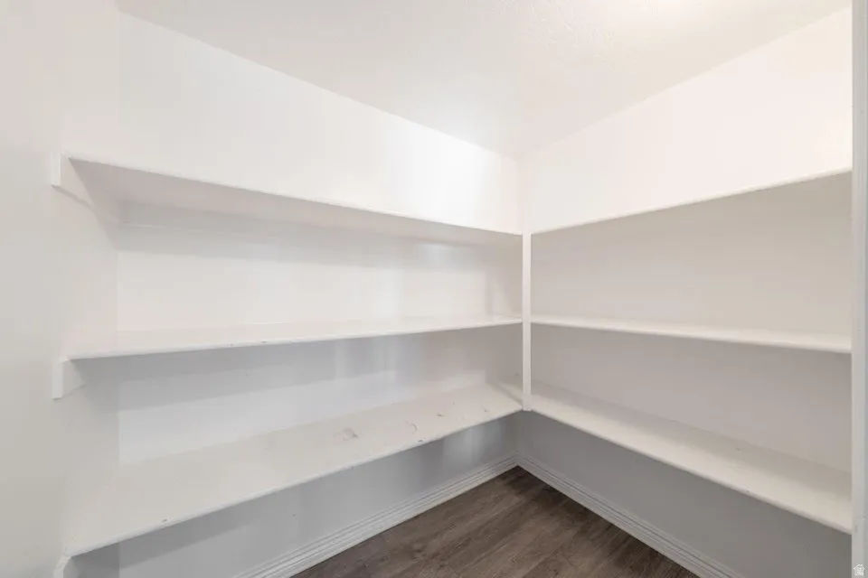Walk-in pantry featuring extensive white shelving and wood-finish flooring