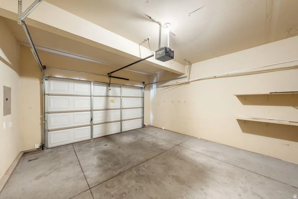 Attached garage with concrete flooring, automatic garage door opener, and built-in shelving