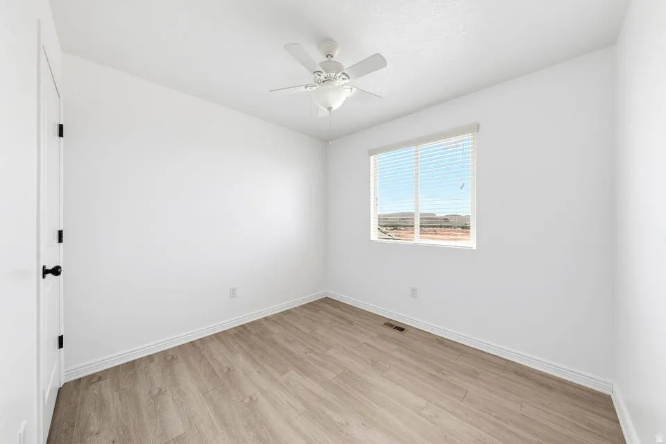 White walls with wood-finish flooring, a ceiling fan, and a window with blinds