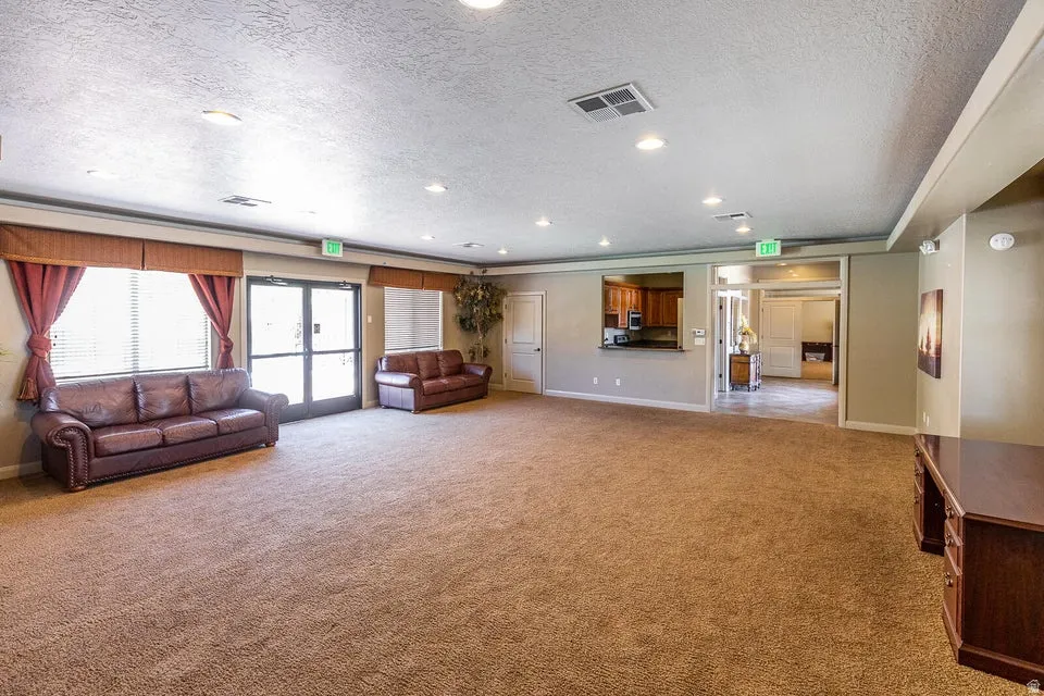 Expansive carpeted area with recessed lighting, multiple windows with blinds, and a pass-through opening to an additional room