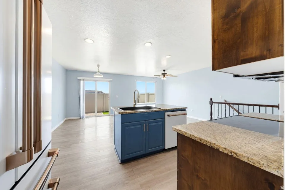 Open-concept kitchen and living area featuring a central island with a sink, stainless steel appliances, light wood-finish flooring, and sliding glass door access to an outdoor area