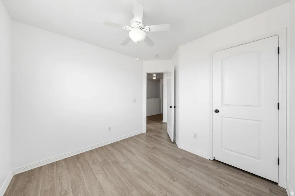 Wood-finish flooring, white walls, ceiling fan, and white paneled doors