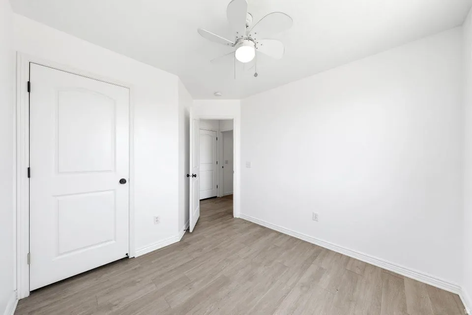 White walls, wood-finish flooring, white paneled doors, and a ceiling fan