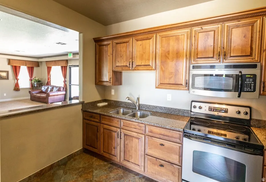 Kitchen featuring wood cabinetry, a stainless steel microwave and oven, a double basin sink, and stone-finish countertops