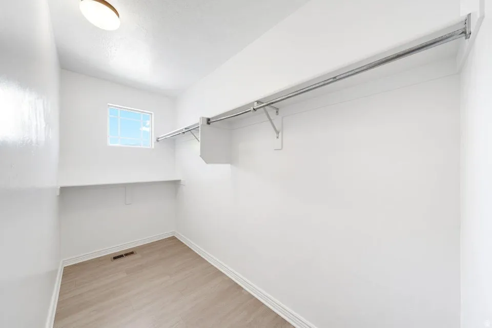 Walk-in closet featuring wood-finish flooring, built-in shelving, and a window