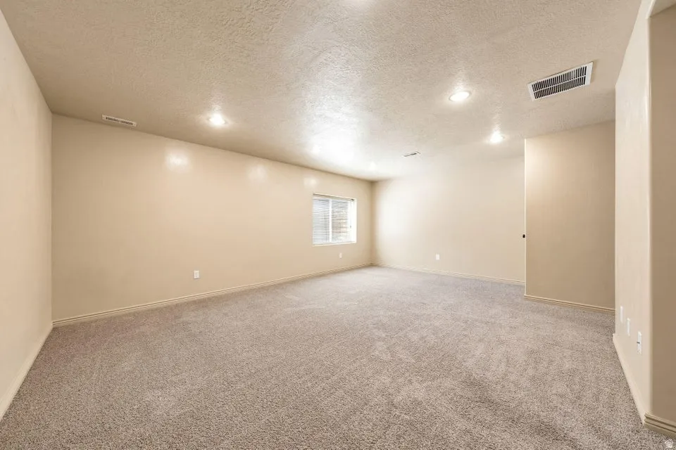 Expansive room featuring recessed lighting, neutral wall paint, textured ceiling, and a window with blinds
