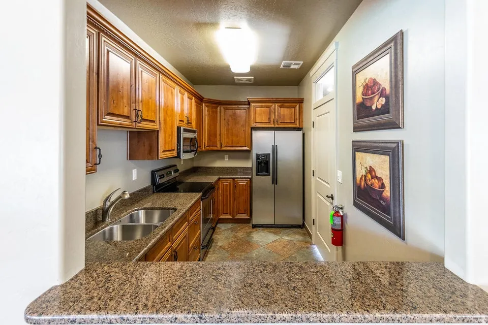 Kitchen featuring wood cabinetry, stainless steel appliances, dual basin sink, stone-finish countertops, and tile flooring