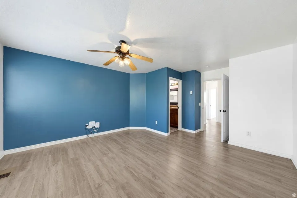 Spacious room featuring wood-finish flooring, a ceiling fan with integrated lighting, and multiple entryways