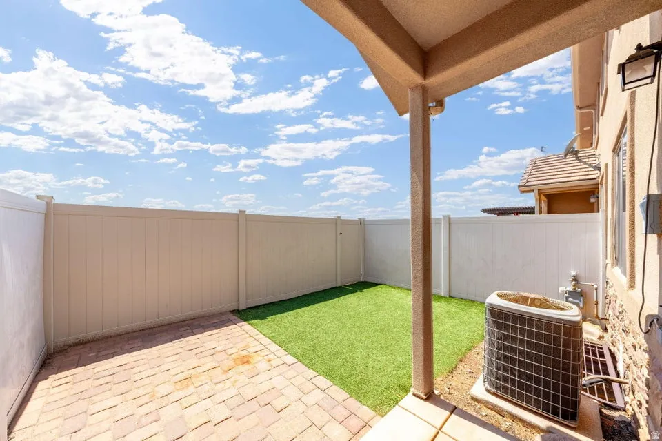 Private patio area featuring a brick paver surface, artificial turf, and full-height privacy fencing